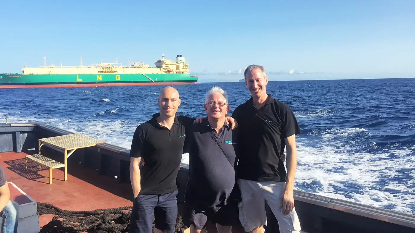3 men on a ship with an LNG vessel in the background.